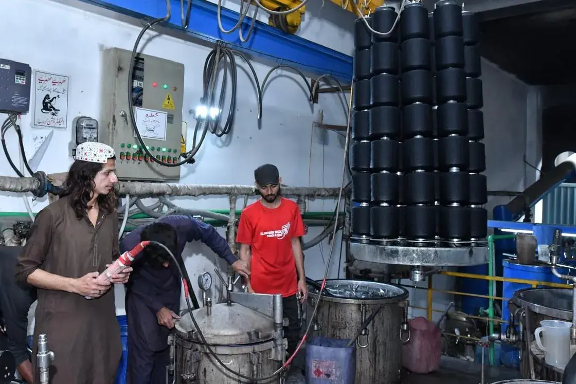 Package dyeing in progress: a carrier of dyed yarn packages on the hoist above two pressurised kiers, with the dosing lines and control panel behind.