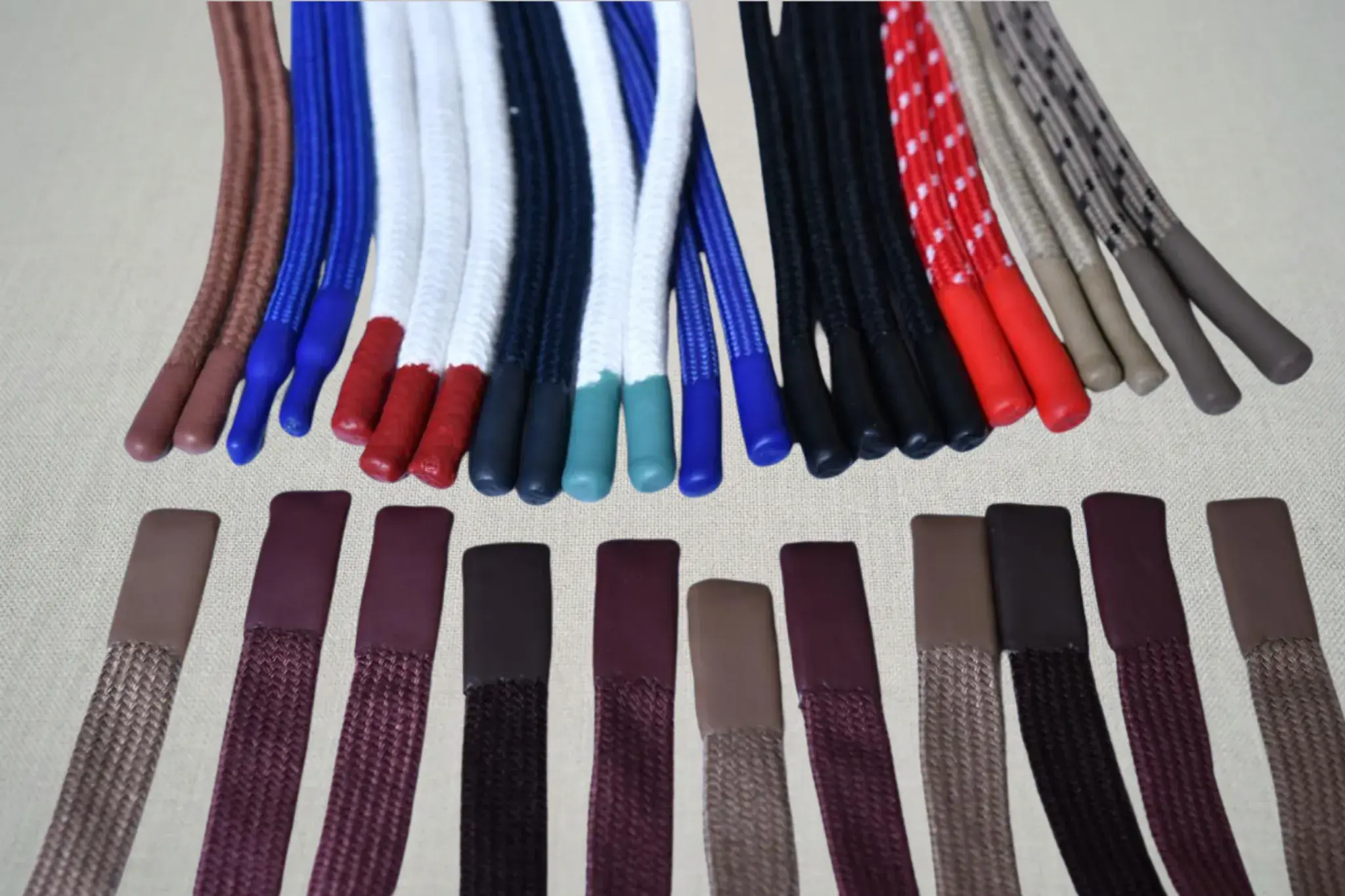 Finished draw cords and flat tapes laid out in rows, each with a moulded tip on the end, in a range of colours.